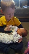 a little boy feeding his newborn sister